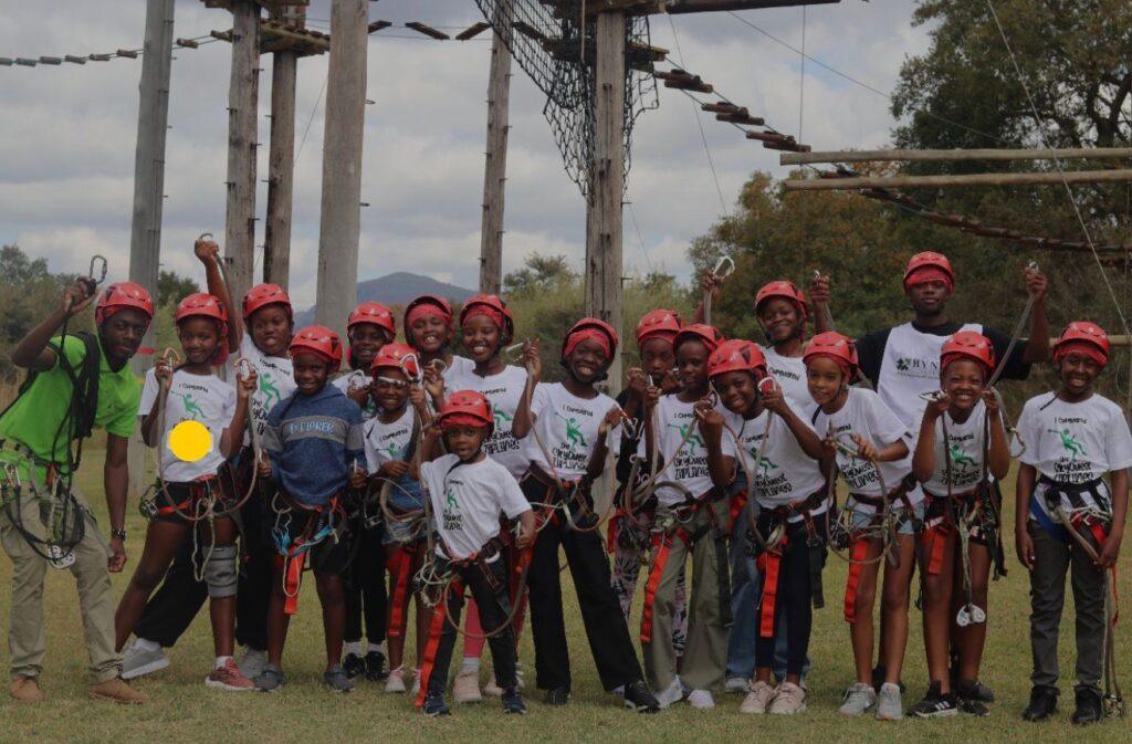 Group in rope gear smiling (team photo) school-rope-course-team-building.jpg students in safety gear during rope course team building activity School Leadership Camps